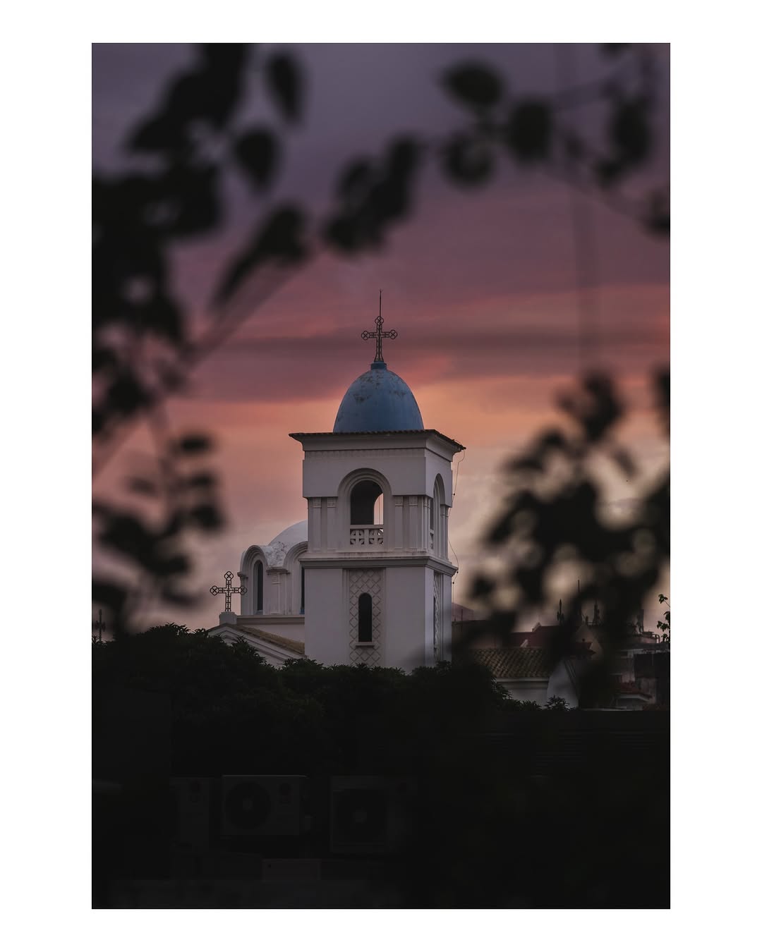 Church with blue dome and cross against a dramatic sunset sky
